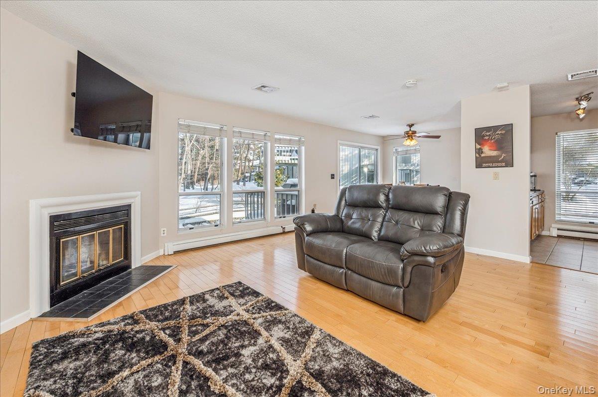 58 Villa Drive Peekskill, NY 10566 - Photo 10 of 21 Living area featuring light wood-style flooring, a tiled fireplace, a baseboard radiator, and plenty of natural light
