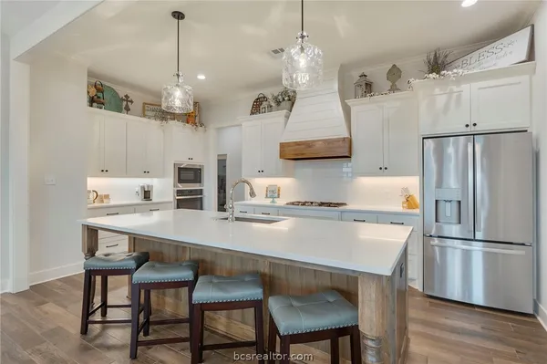 a kitchen with stainless steel appliances granite countertop a sink a stove a refrigerator and chairs