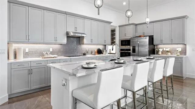 a kitchen with stainless steel appliances a sink a stove a refrigerator cabinets and chairs