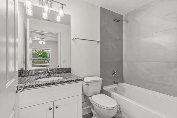 a bathroom with a granite countertop sink toilet mirror and bathtub