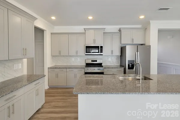 a kitchen with granite countertop a refrigerator a sink and white cabinets