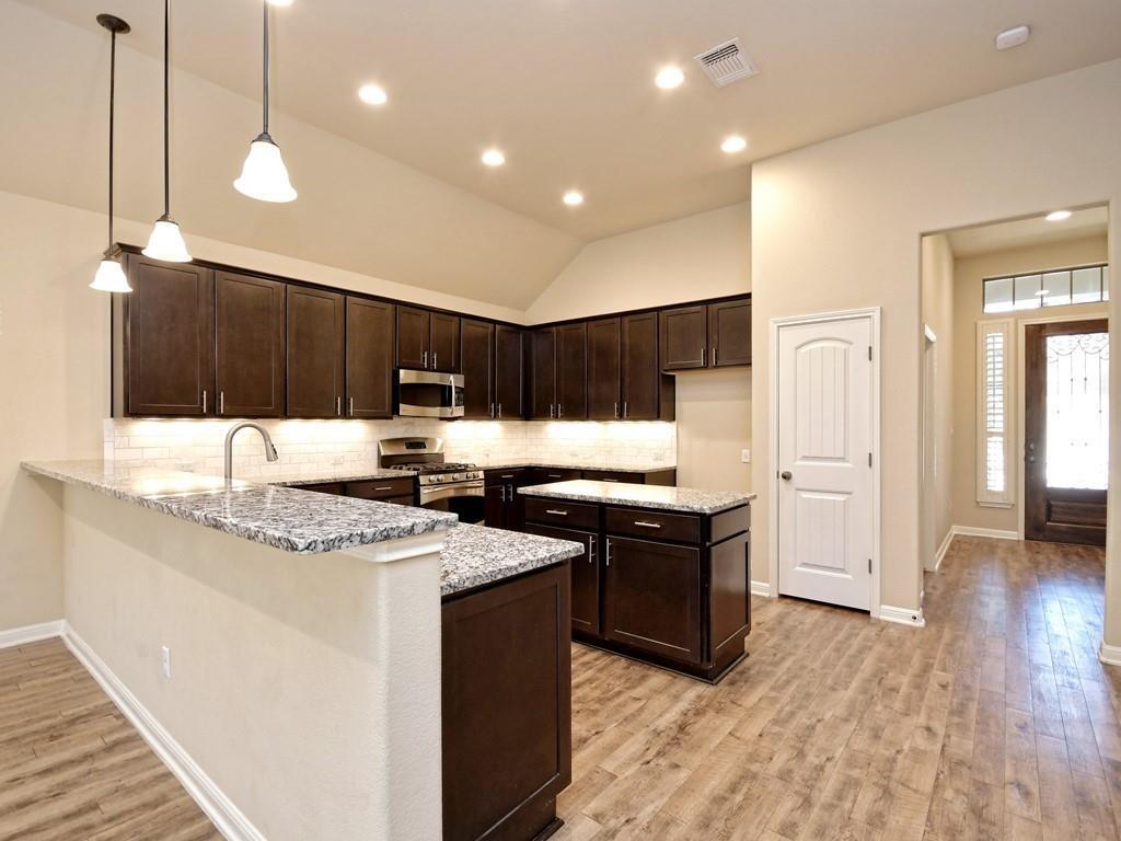 2216 Lookout Range Drive Leander, TX 78641 - Photo 5 of 16 Kitchen with dark brown cabinets, a peninsula, pendant lighting, light stone counters, and lofted ceiling