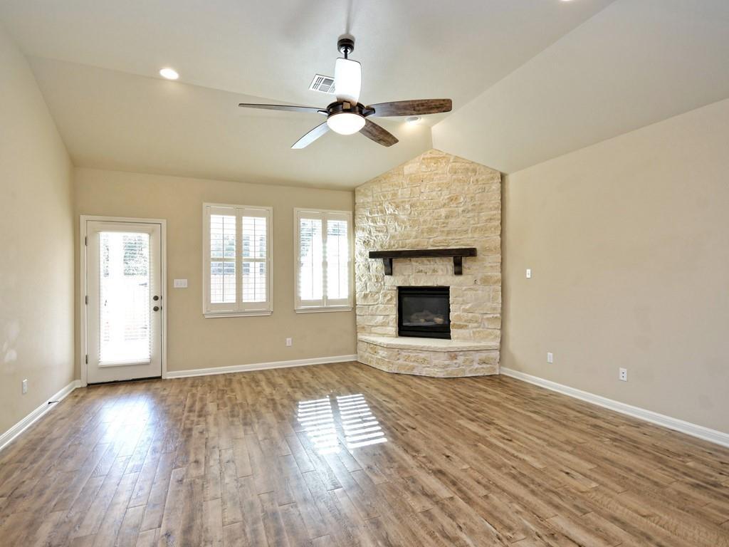 2216 Lookout Range Drive Leander, TX 78641 - Photo 8 of 16 Unfurnished living room featuring vaulted ceiling, a stone fireplace, light wood-style flooring, and ceiling fan