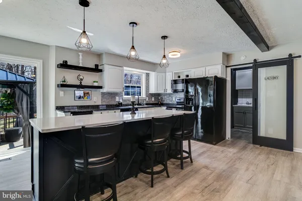 a kitchen with stainless steel appliances granite countertop a refrigerator a sink dishwasher a stove a dining table and chairs with wooden floor