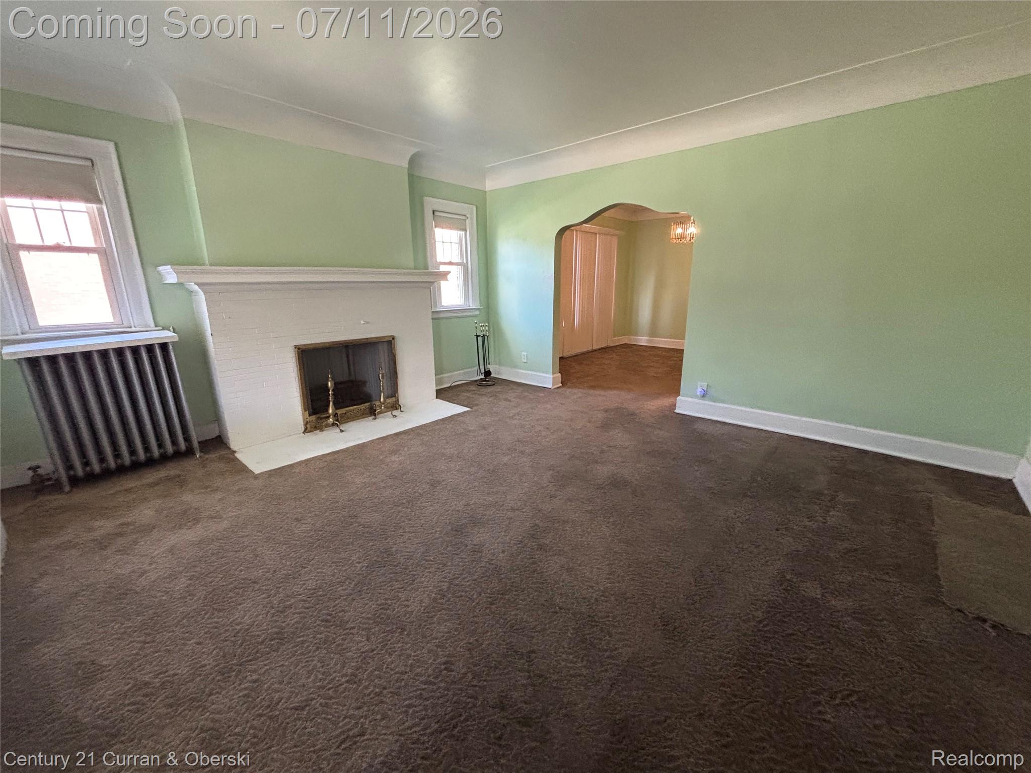 3237 Calvert Avenue Detroit, MI 48206 - Photo 2 of 8 Interior room featuring a fireplace with a white mantel and hearth, windows with natural light, and a curved archway opening to an additional room with wood-finish flooring