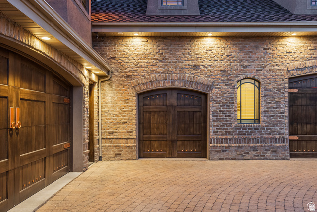 694 West Cephus Road Draper, UT 84020 - Photo 131 of 148 Stone and brick facade with arched wood-finish garage doors, accented by sconce lighting and an arched window with decorative ironwork