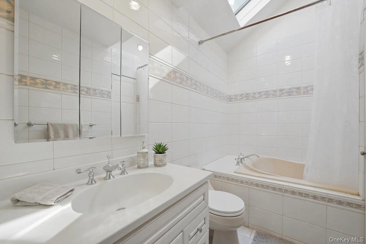 29 Montrose Road Yonkers, NY 10710 - Photo 13 of 39 2nd floor bathroom featuring a white tile surround, decorative accent tile band, white vanity with integrated sink, chrome faucet, and mirrored medicine cabinet