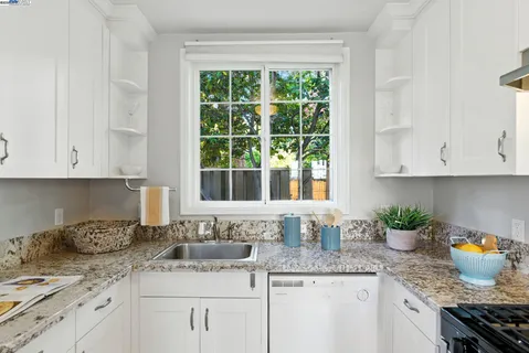 a kitchen with granite countertop stainless steel appliances a sink a window and white cabinets