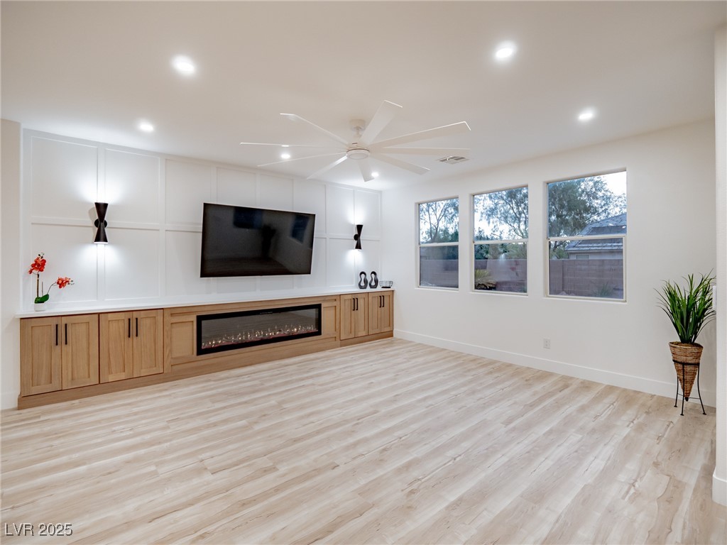 7870 Midnight Ride Street Las Vegas, NV 89131 - Photo 25 of 69 Unfurnished living room featuring ceiling fan, light wood-style flooring, a decorative wall, a glass covered fireplace, and recessed lighting