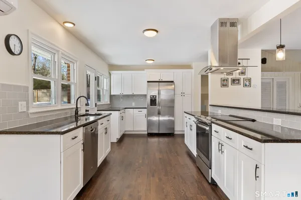 a kitchen with stainless steel appliances granite countertop a stove top oven a sink a refrigerator and white cabinets with wooden floor