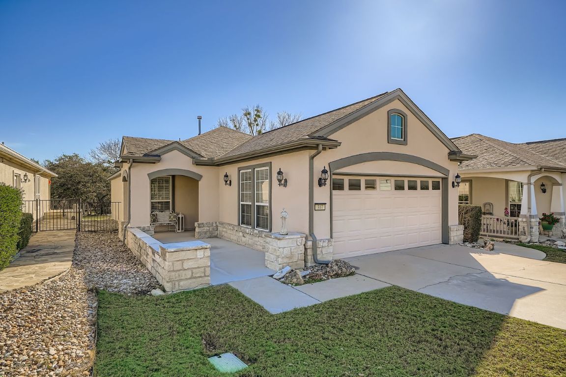 View of front of home with stucco siding, driveway, stone siding, a gate, and a garage