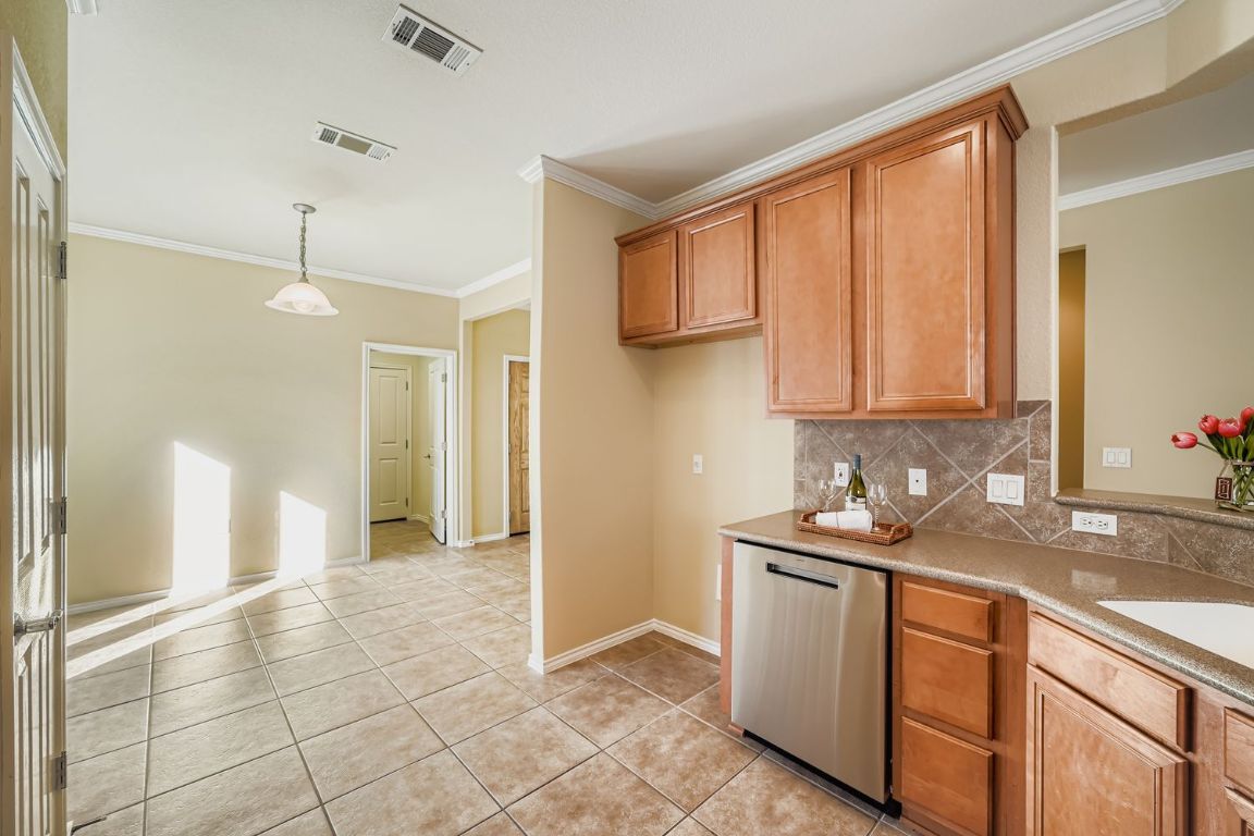 307 Mill Pond Path Georgetown, TX 78633 - Photo 11 of 26 Kitchen featuring stainless steel dishwasher, tasteful backsplash, brown cabinets, ornamental molding, and hanging light fixtures