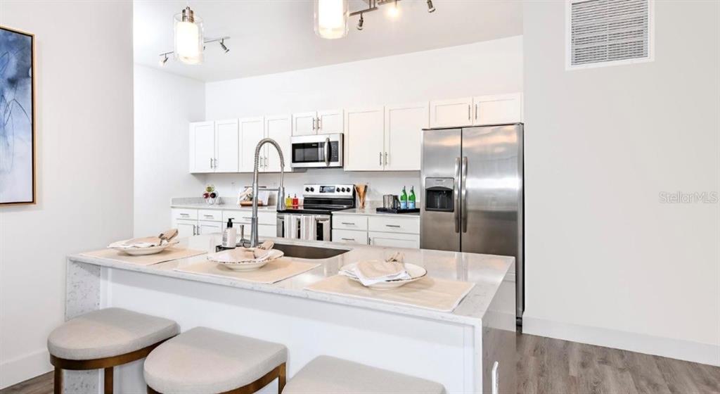 a kitchen with stainless steel appliances kitchen island granite countertop a sink a refrigerator and white cabinets