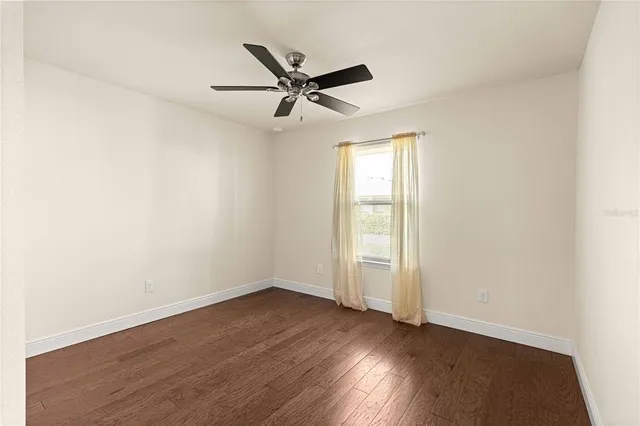 an empty room with wooden floor chandelier fan and windows