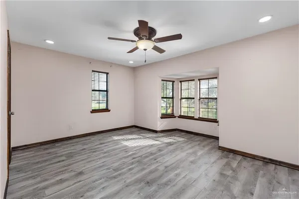 an empty room with wooden floor chandelier fan and windows