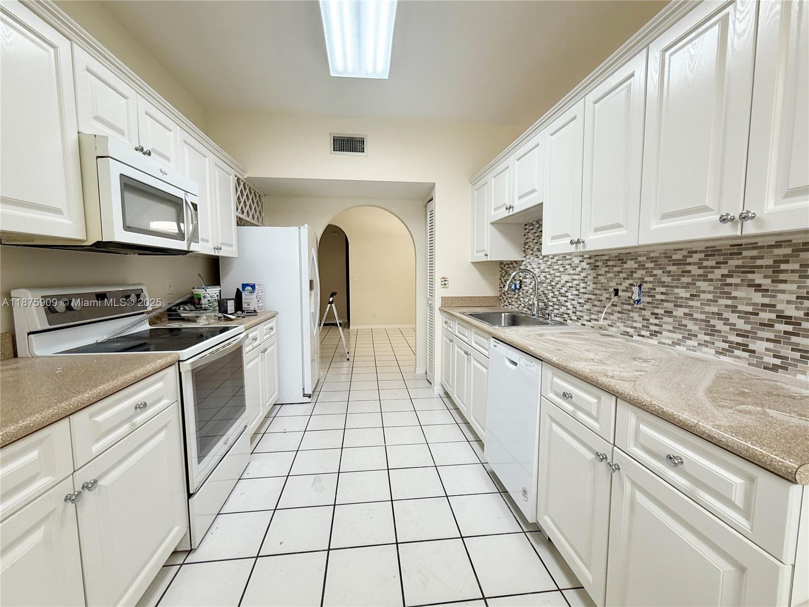 8658 Vía Reale, Unit 3 Boca Raton, FL 33496 - Photo 11 of 39 a kitchen with white cabinets a sink dishwasher and a stove with wooden floor