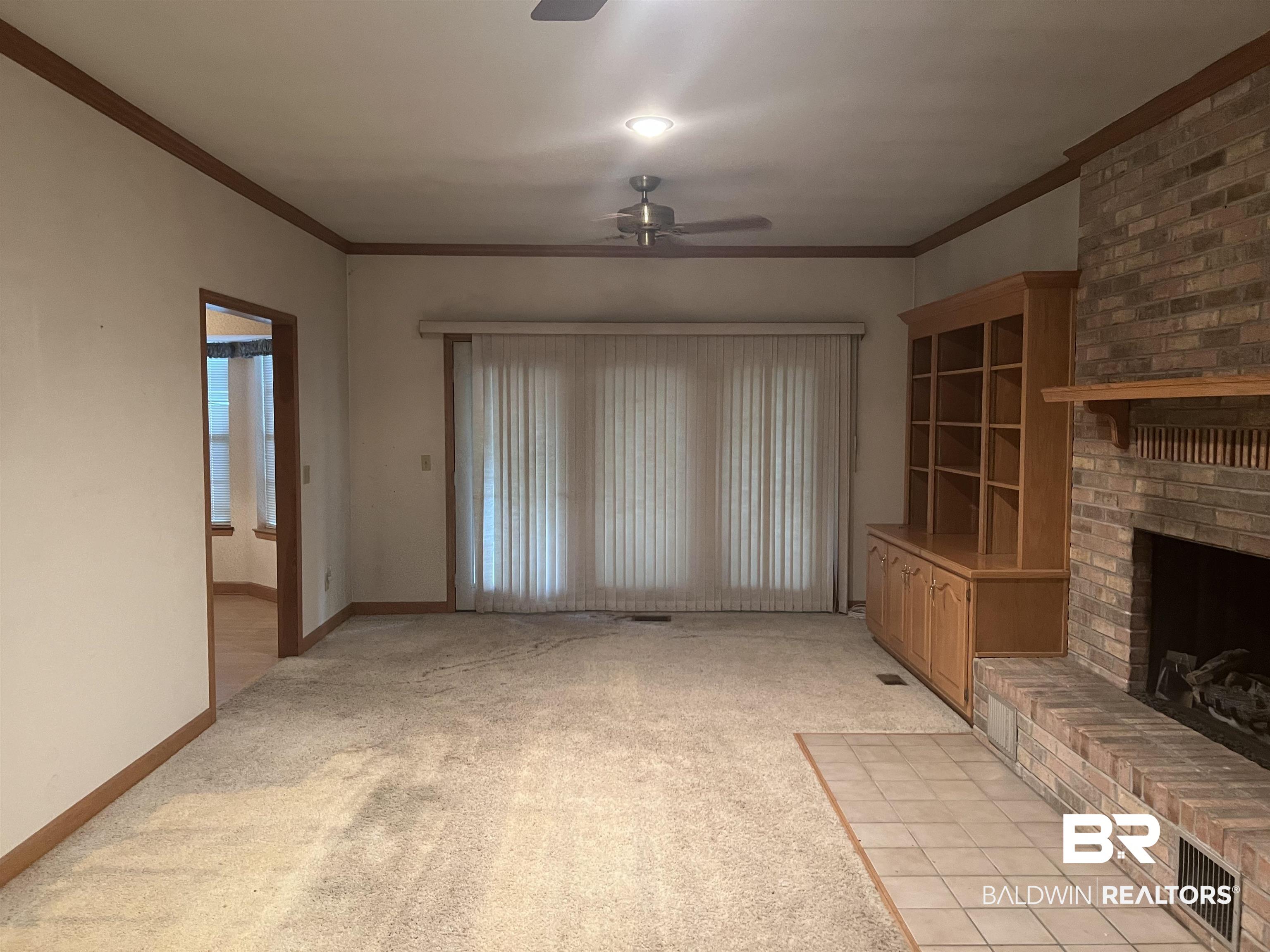 295 Norwood Road Monroeville, AL 36460 - Photo 3 of 32 Unfurnished living room with a ceiling fan, light colored carpet, a brick fireplace, crown molding, and baseboards