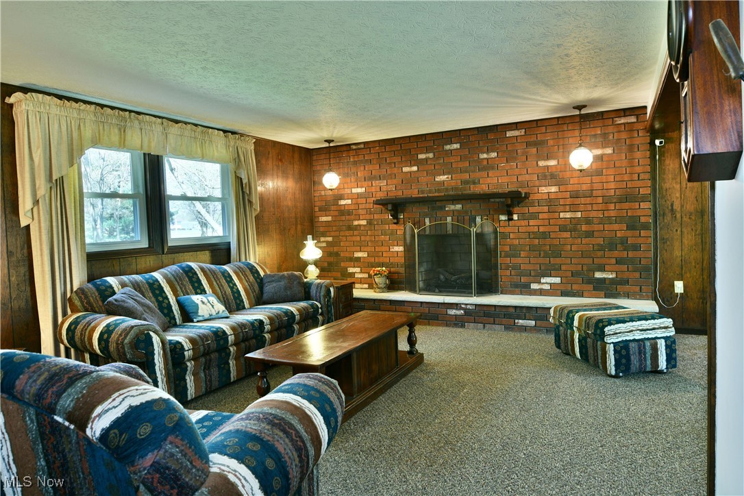 379 Housel Craft Road Bristolville, OH 44402 - Photo 37 of 50 Carpeted living area with a textured ceiling, a brick fireplace, brick wall, and wooden walls
