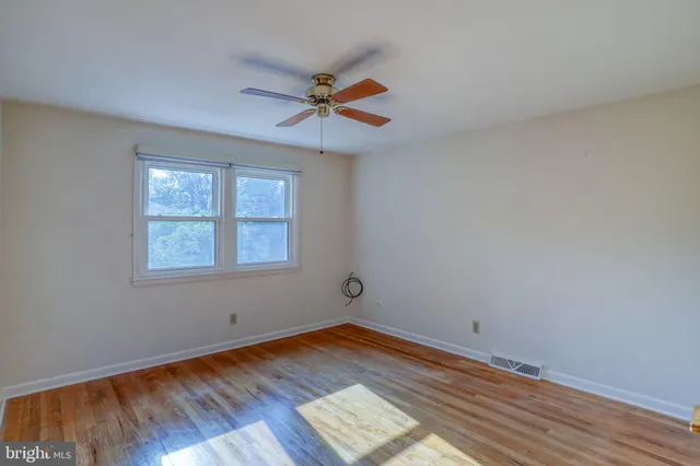 a view of empty room with wooden floor and fan