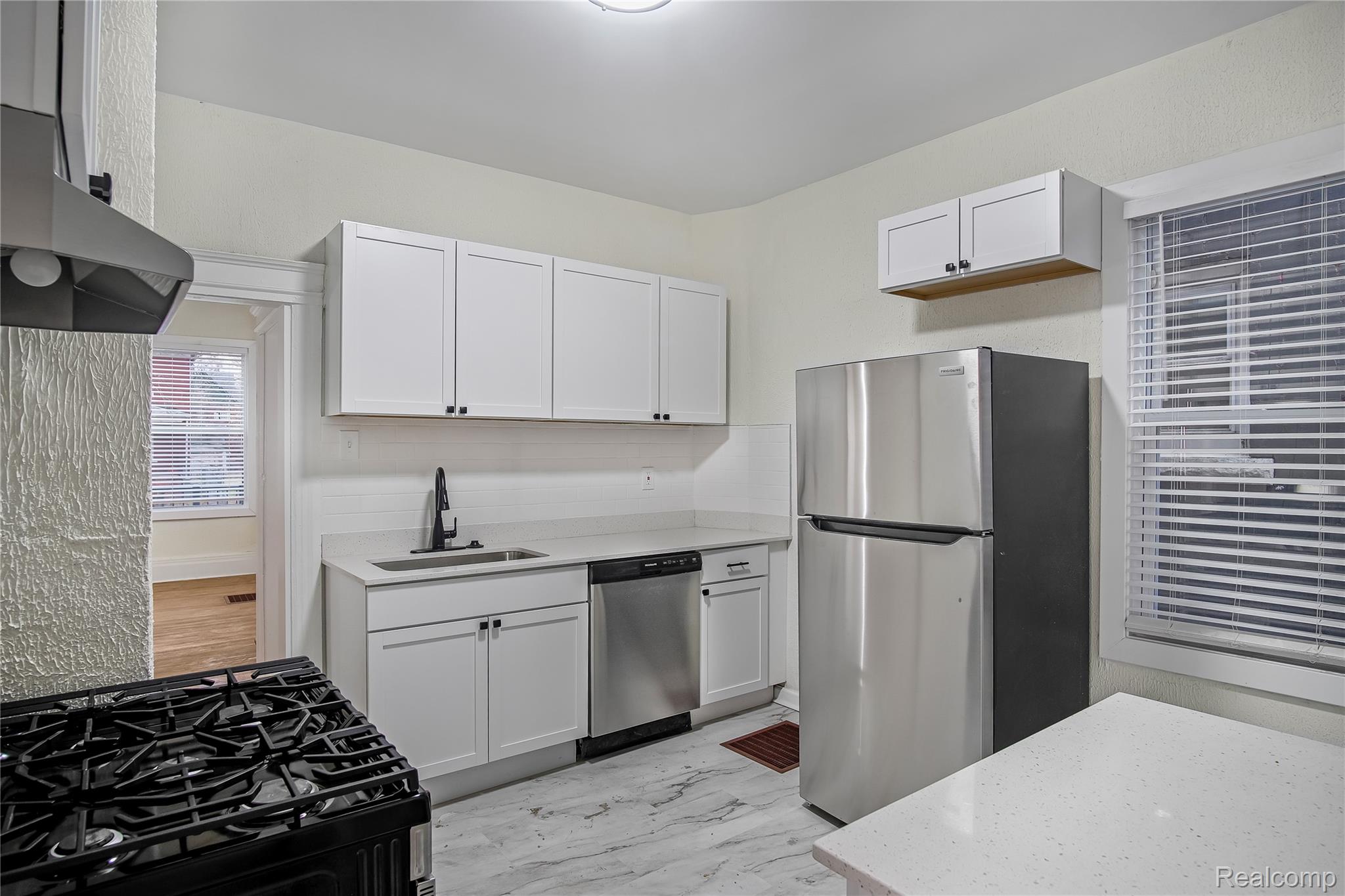 427 Melbourne Street Detroit, MI 48202 - Photo 5 of 29 Kitchen with appliances with stainless steel finishes, light marble finish flooring, white cabinetry, under cabinet range hood, and light stone counters