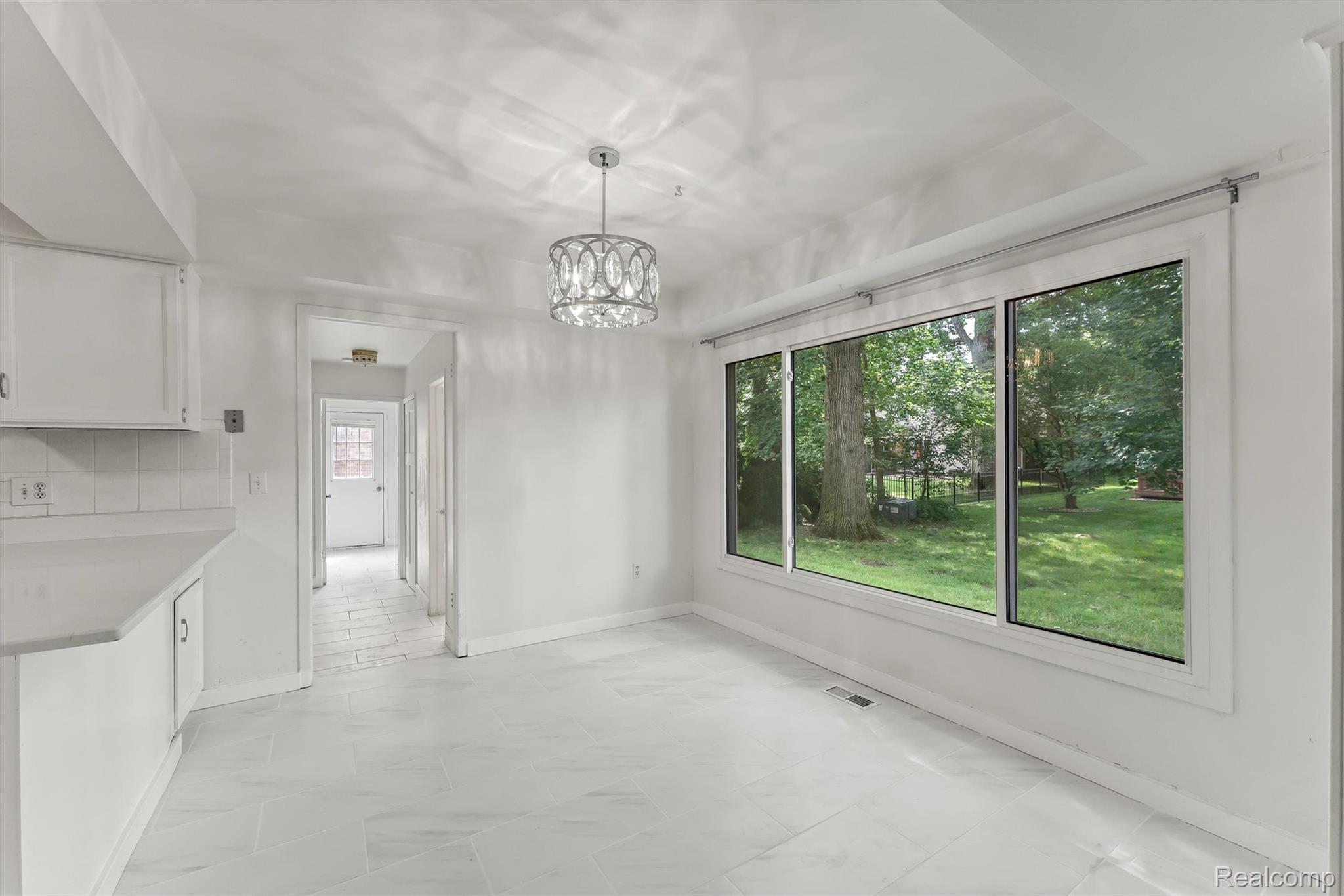 2118 Rutgers Drive Troy, MI 48085 - Photo 12 of 39 Bright interior space featuring a large three-panel window overlooking a green yard, tile flooring, a modern chandelier, white cabinetry, and a subway tile backsplash