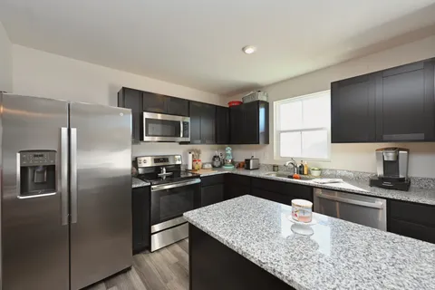 a kitchen with kitchen island granite countertop stainless steel appliances a sink stove refrigerator and cabinets