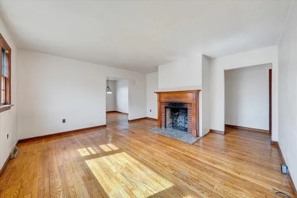 a view of an empty room with wooden floor fireplace and a window