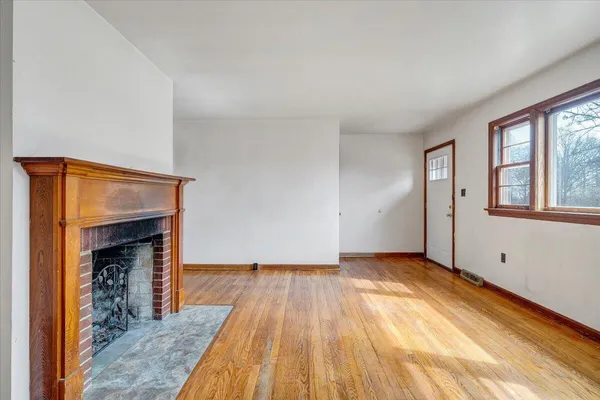 an empty room with wooden floor fireplace and windows