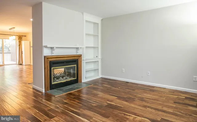 a view of an empty room with wooden floor fireplace and a window