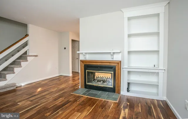 a view of an empty room with wooden floor fireplace and a window