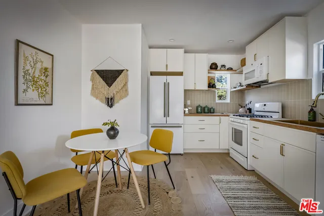 a kitchen with stainless steel appliances granite countertop a white refrigerator a stove a dining table and chairs with wooden floor