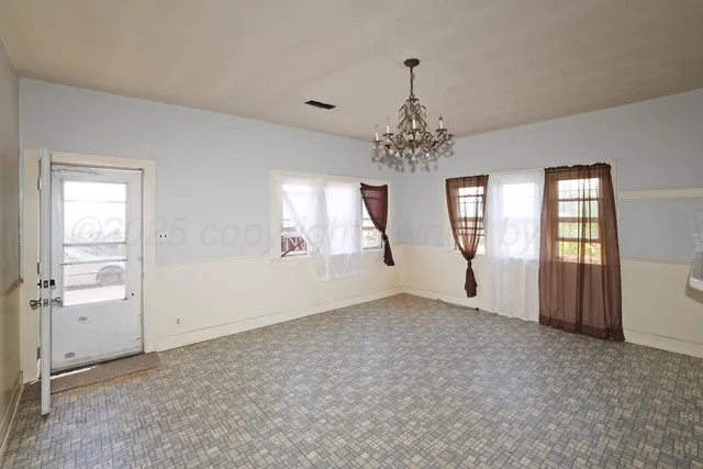an empty room with chandelier and windows