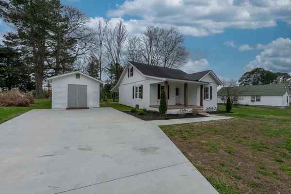 a view of a white house next to a yard with big trees and wooden fence