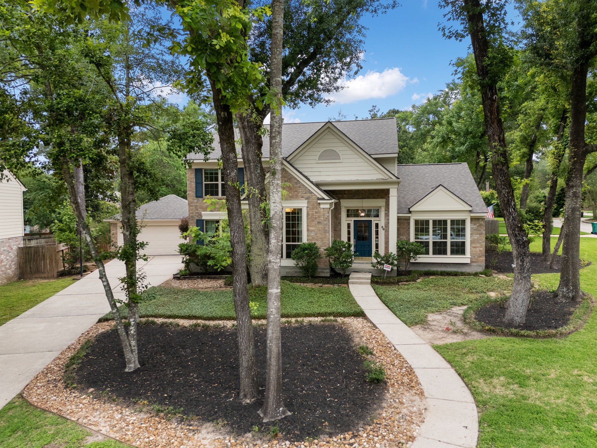 59 Fire Flicker Place Spring, TX 77381 - Photo 35 of 37 Charming two-story home with a brick facade, nestled among mature trees. Features a welcoming walkway, lush landscaping, and a spacious driveway. Ideal for those seeking a serene, suburban setting.