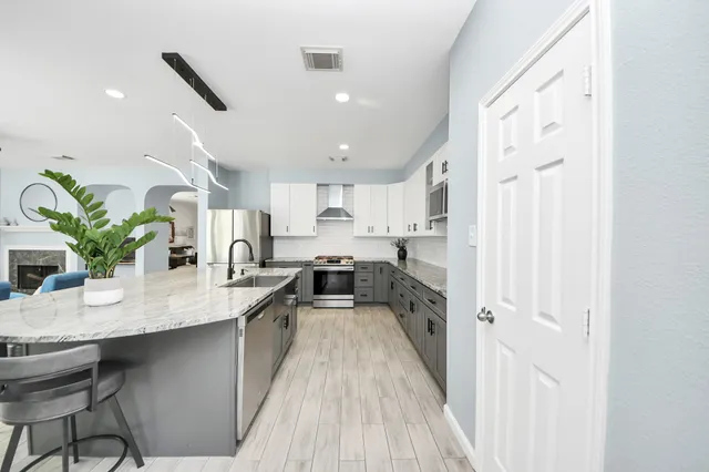 a kitchen with stainless steel appliances granite countertop a refrigerator a sink dishwasher and white cabinets with wooden floor