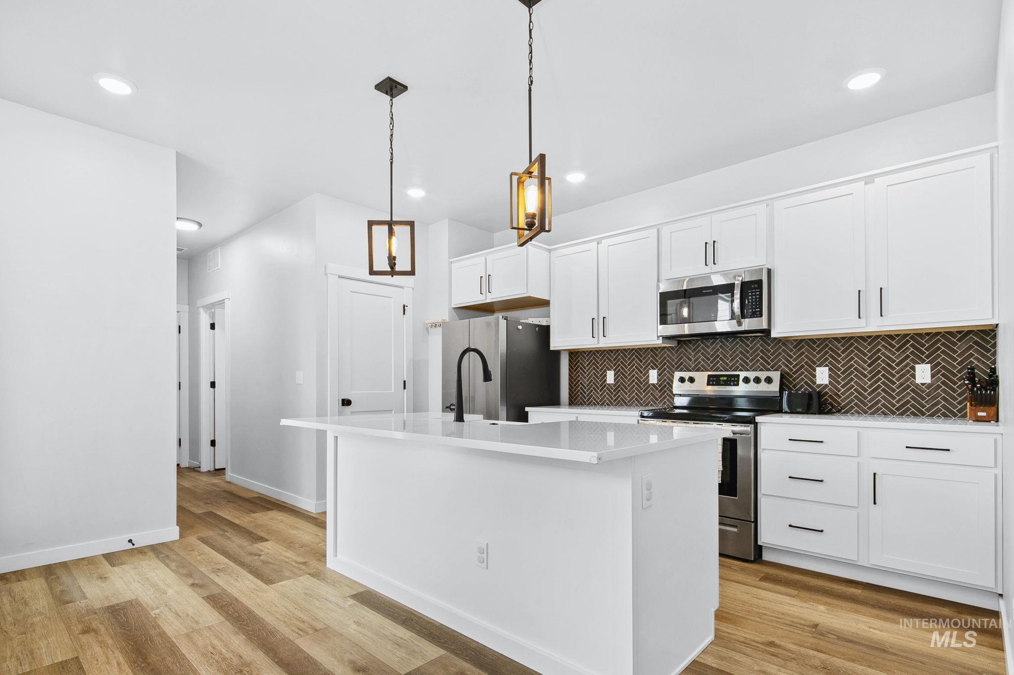 298 South Fritts Avenue Meridian, ID 83642 - Photo 9 of 32 Kitchen featuring stainless steel appliances, white cabinetry, an island with sink, decorative light fixtures, and light wood-type flooring