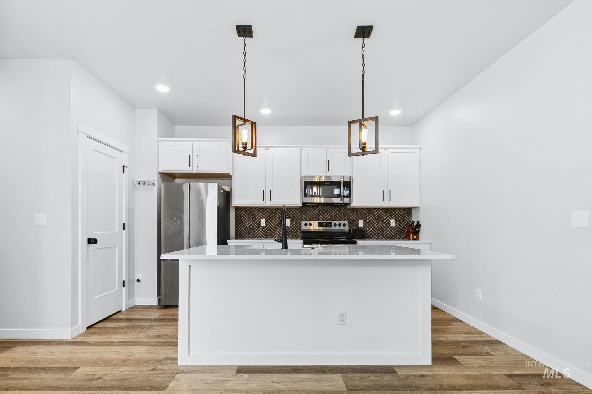 298 South Fritts Avenue Meridian, ID 83642 - Photo 10 of 32 Kitchen featuring white cabinets, stainless steel appliances, a kitchen island with sink, and light wood-style floors