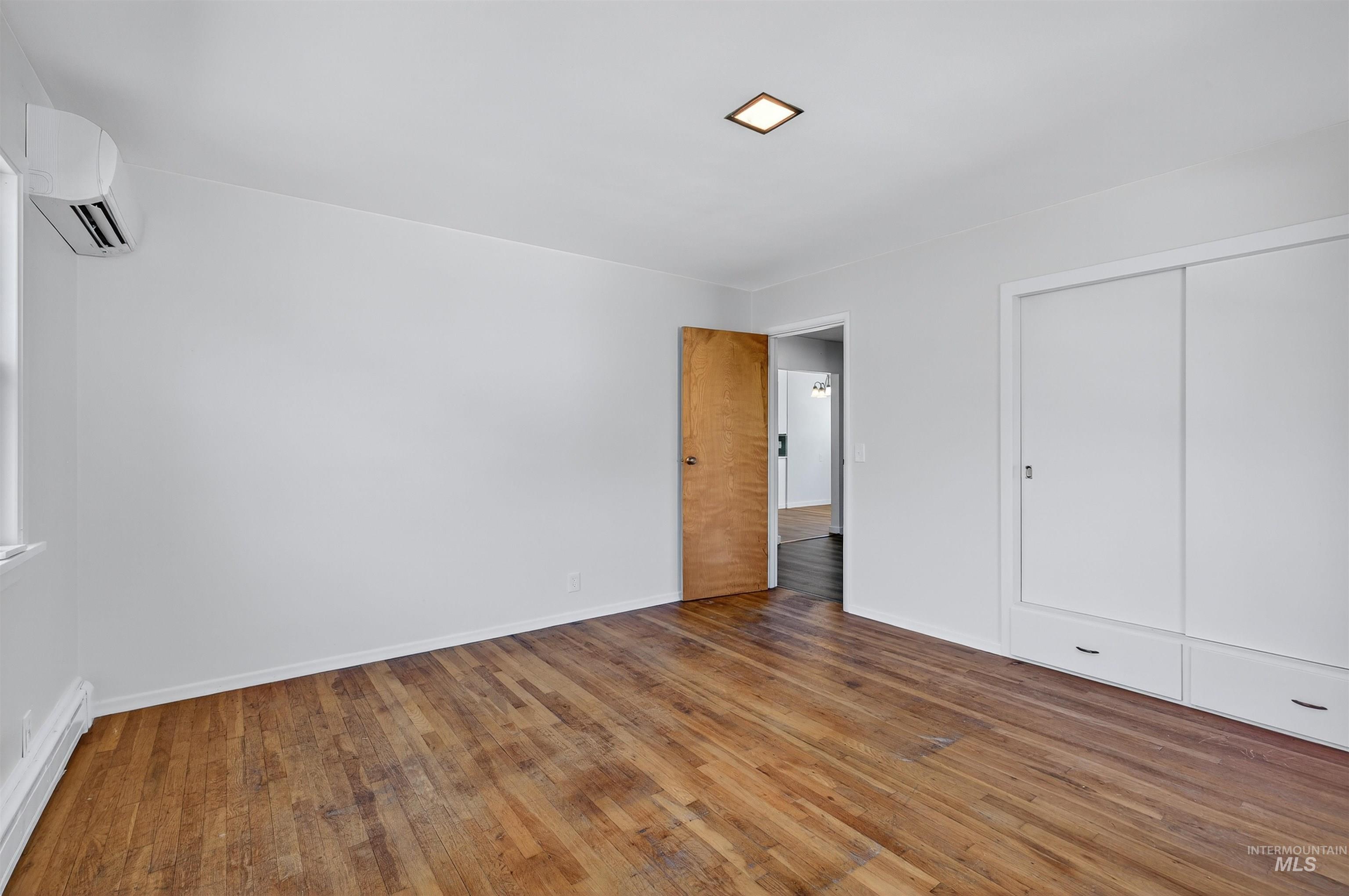 164 State Street Juliaetta, ID 83535 - Photo 13 of 37 Unfurnished bedroom featuring a baseboard radiator, hardwood / wood-style flooring, a wall mounted air conditioner, and a closet