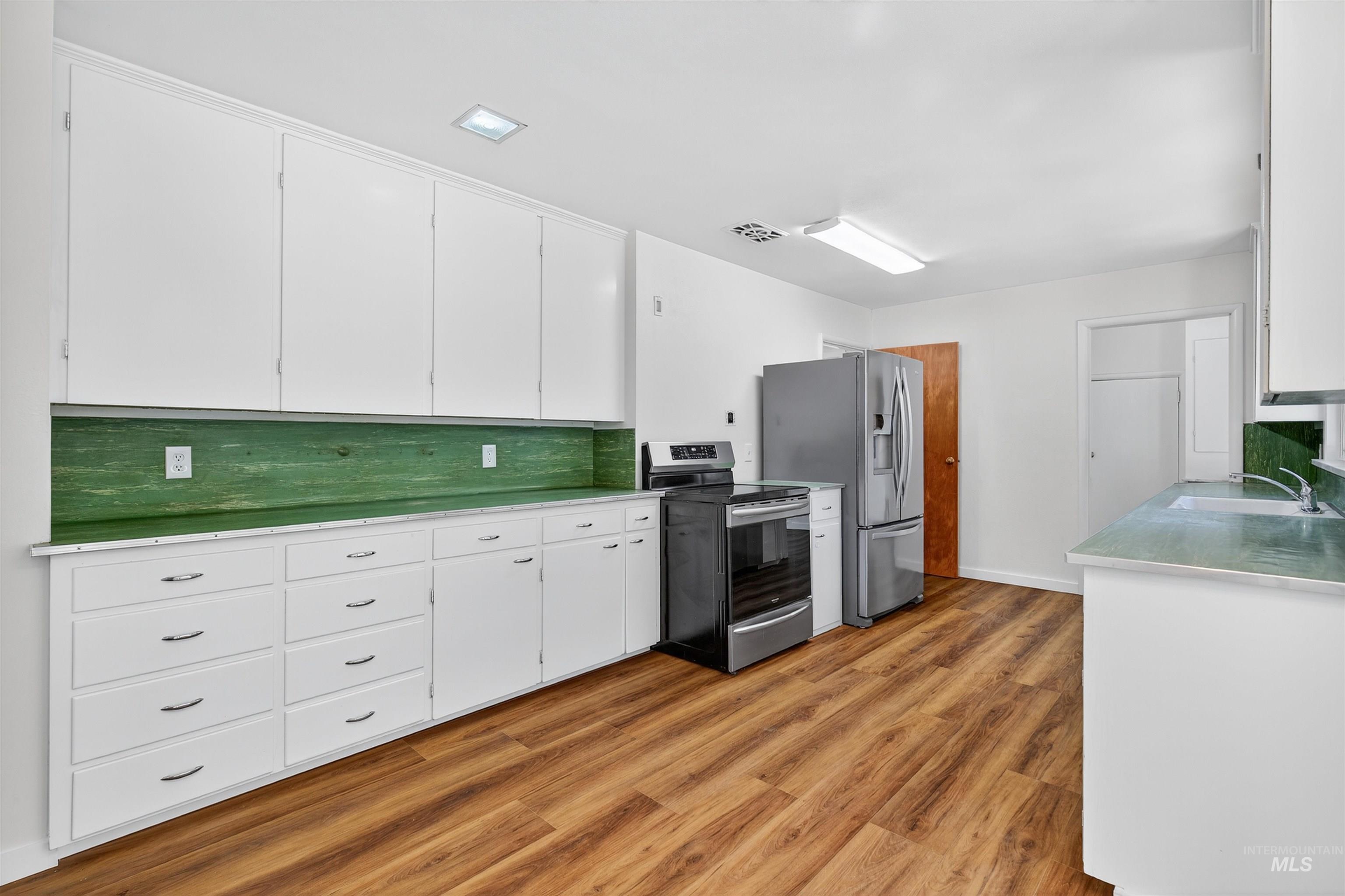 164 State Street Juliaetta, ID 83535 - Photo 14 of 37 Kitchen with electric stove, decorative backsplash, light wood-style flooring, light countertops, and white cabinets