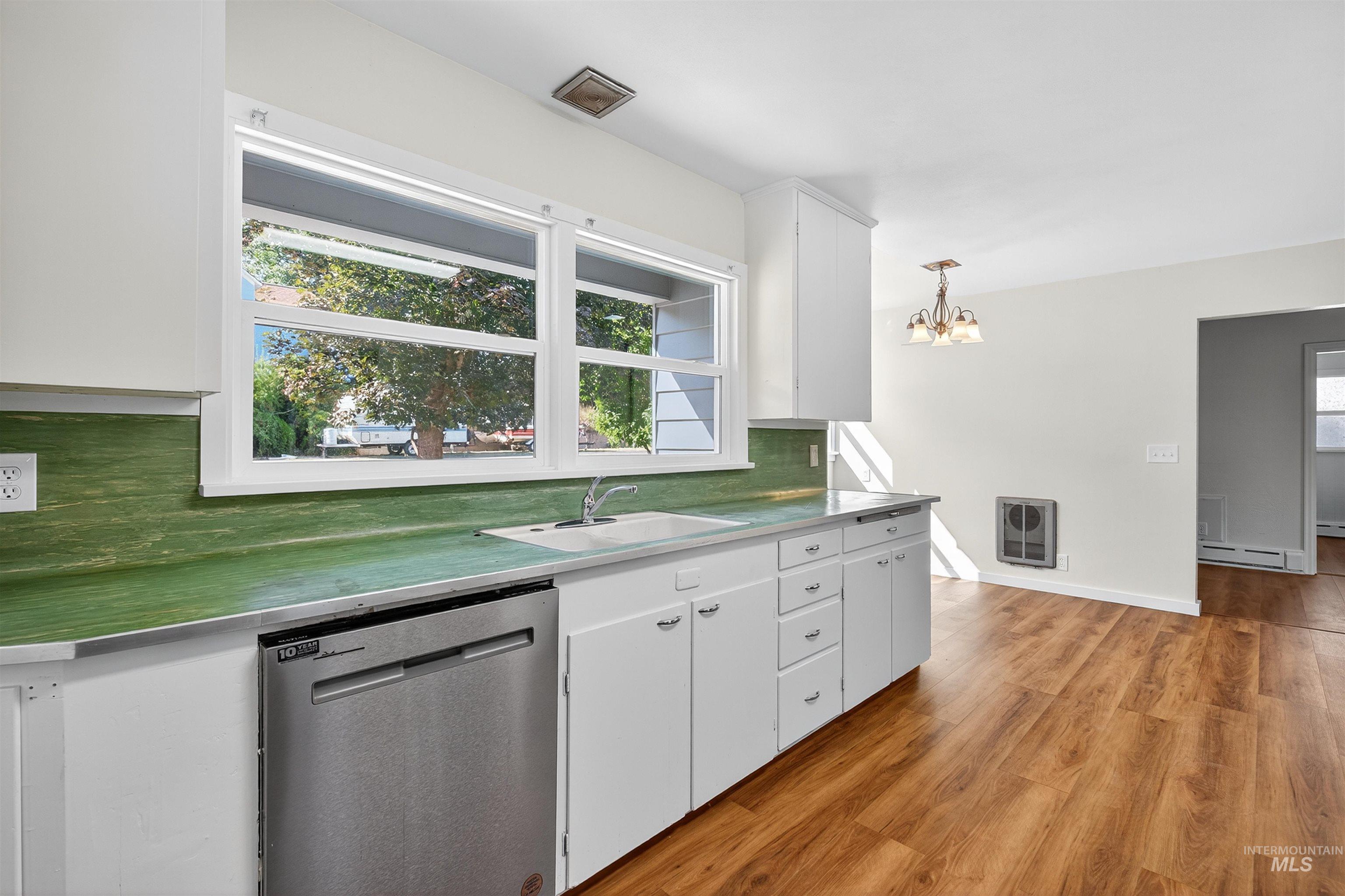 164 State Street Juliaetta, ID 83535 - Photo 16 of 37 Kitchen with stainless steel dishwasher, white cabinets, tasteful backsplash, light wood-type flooring, and a chandelier
