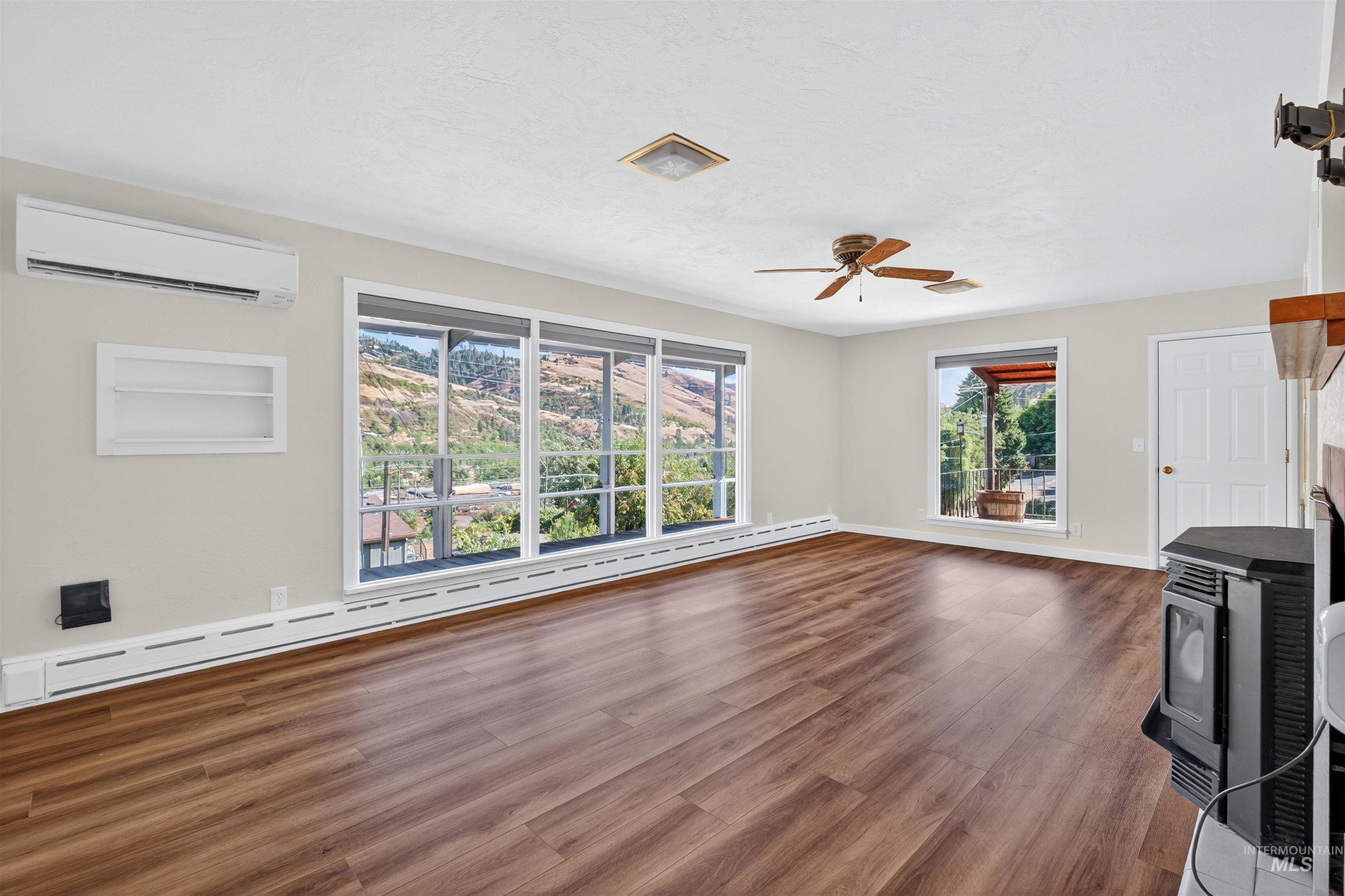 164 State Street Juliaetta, ID 83535 - Photo 18 of 37 Unfurnished living room with a wood stove, a baseboard radiator, dark wood-type flooring, a wall unit AC, and a ceiling fan