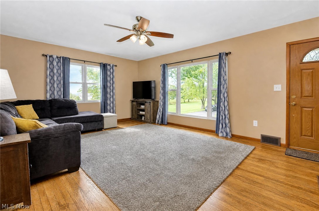 3864 State Road South Ashtabula, OH 44004 - Photo 11 of 50 Hardwood flooring, ceiling fan with integrated lighting, multiple windows providing natural light, and a wood-finish entry door with decorative glass
