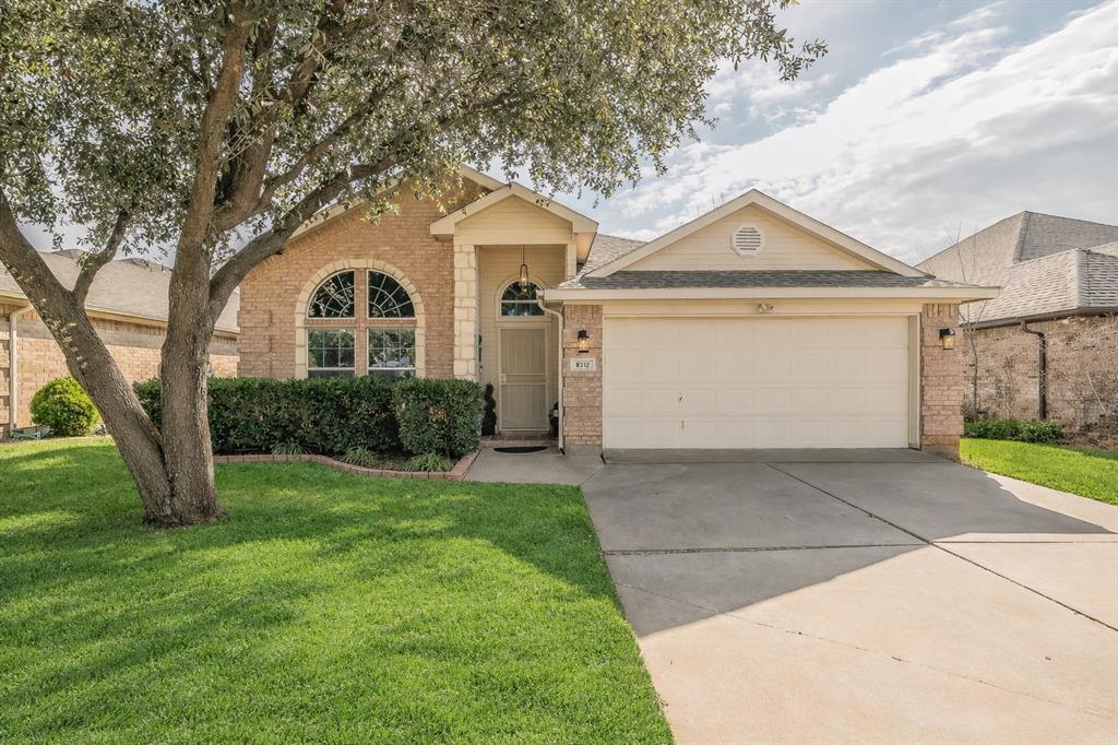 Single-story brick home with attached 2-car garage, front lawn, concrete driveway, arched front window, covered entry, and shingle roof.