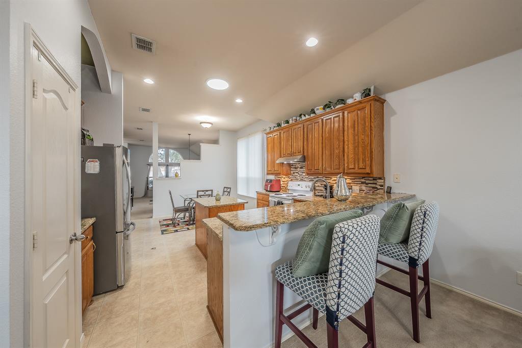 8312 Trinity Vista Trail Hurst, TX 76053 - Photo 18 of 37 Kitchen with a center island, wood finish cabinets, light stone countertops, freestanding refrigerator, and a kitchen bar