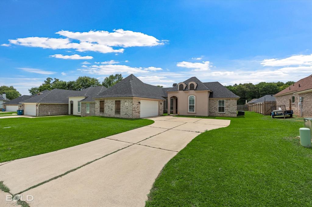 Exterior featuring a light stucco facade, brick accents, multiple gabled rooflines, two front-facing garage doors, and a concrete driveway