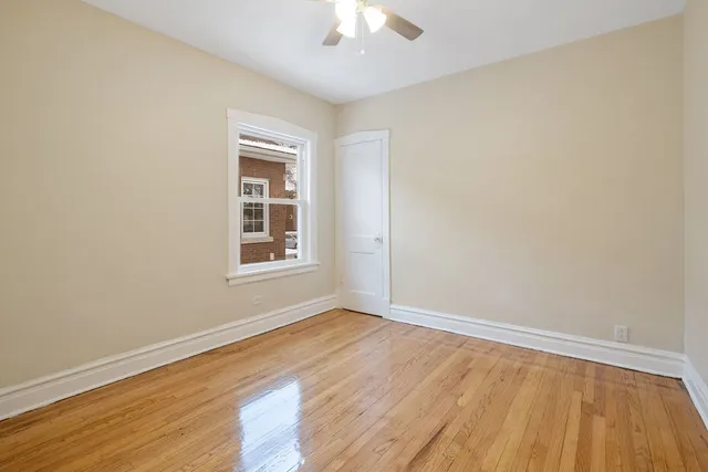 an empty room with wooden floor chandelier fan and windows