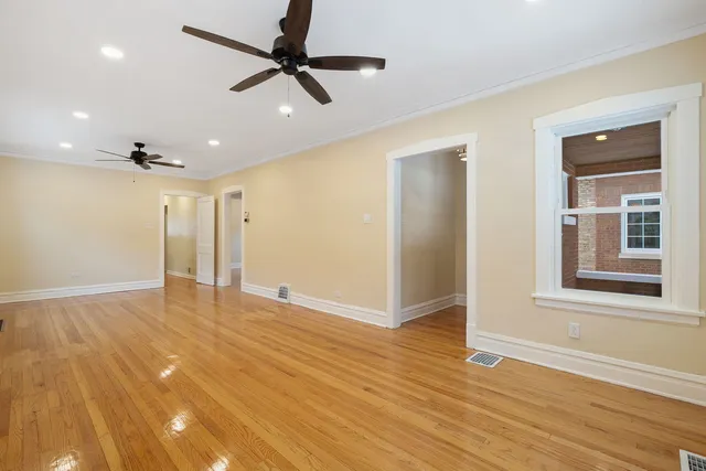 a view of an empty room with wooden floor and a ceiling fan