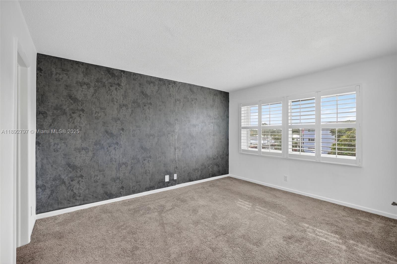 900 Southwest 12th Street, Unit 305 Fort Lauderdale, FL 33315 - Photo 10 of 72 Primary Bedroom w/ Impact Windows, louvered shutters, wallpapered feature wall and newer carpet in amazing condition leading to ensuite bathroom and walk in closet