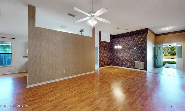 a view of an empty room with wooden floor and a ceiling fan