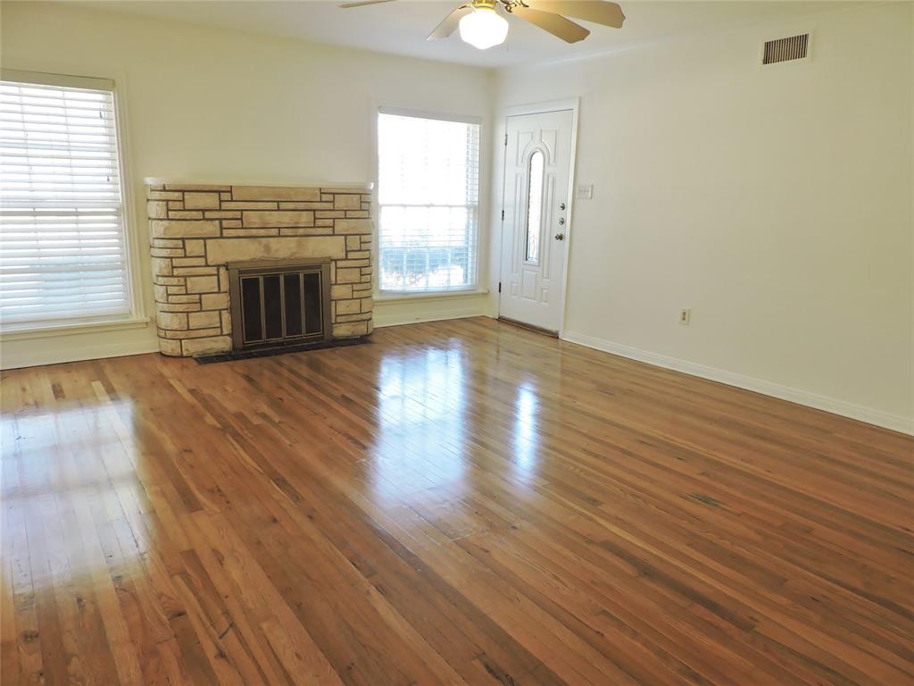 Unfurnished living room featuring a stone fireplace, wood-type flooring, and a ceiling fan